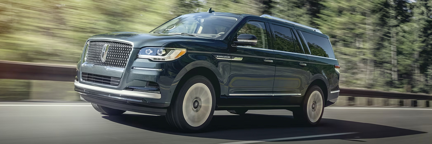 A 2024 Lincoln Navigator® SUV in Flight Blue is being driven up an incline surrounded by greenery.