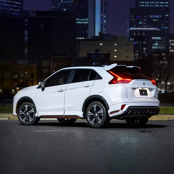 Angled rear view of a white 2023 / 2024 Mitsubishi Eclipse Cross Compact SUV driving in the city at night