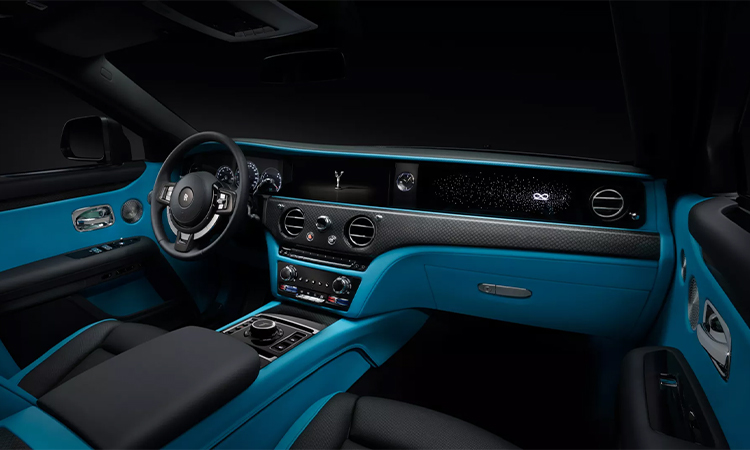 Interior shot of Black Badge Ghost displaying the crisp blue interior, the elegant dashboard and one of a kind steering wheel with the Rolls Royce logo