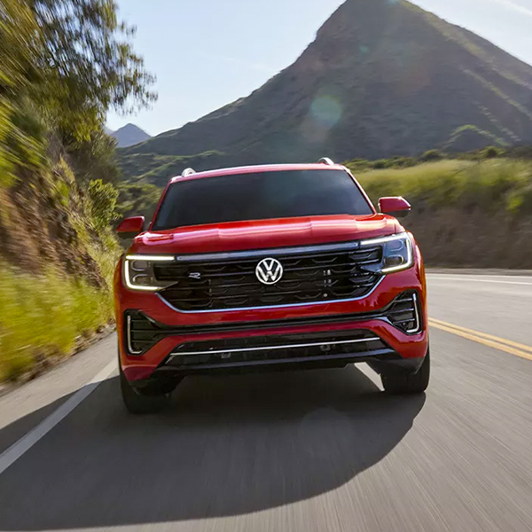 Front view of an Atlas in Aurora Red Metallic driving on a wooded mountain road.