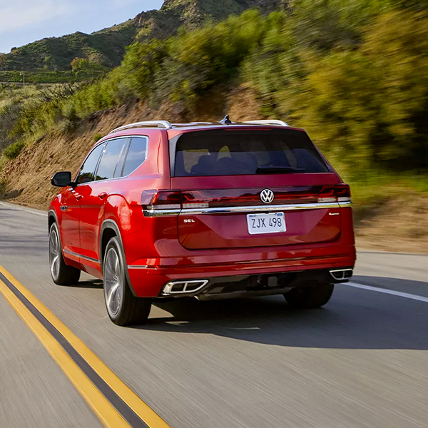 Rear view of an Atlas in Aurora Red Metallic driving on a wooded mountain road.