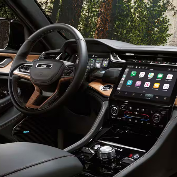 The interior of a 2025 Jeep Grand Cherokee Summit Reserve focusing on the steering wheel, Uconnect touchscreen, center stack and front passenger touchscreen.