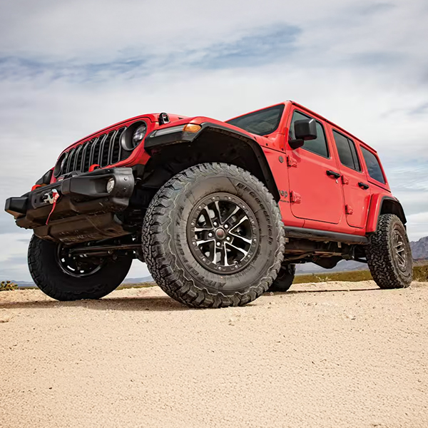 Display A low front angle of a red 2025 Jeep Wrangler Rubicon X parked on sand, with mountains in the background.