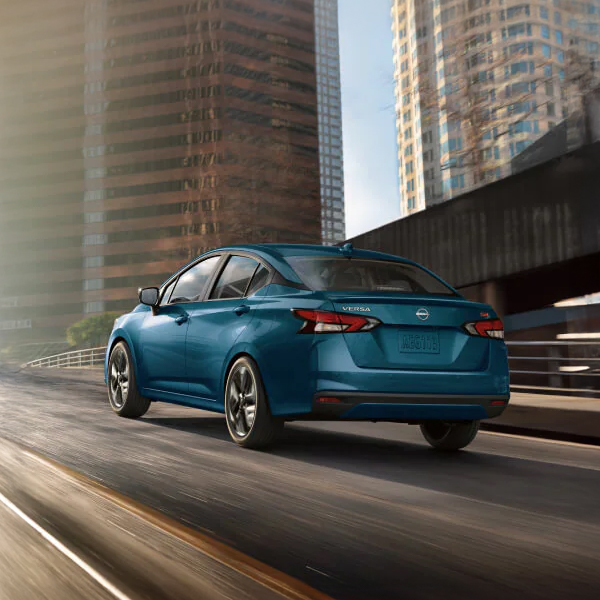2025 Nissan Versa driving down a city highway with tall skyscrapers in the background