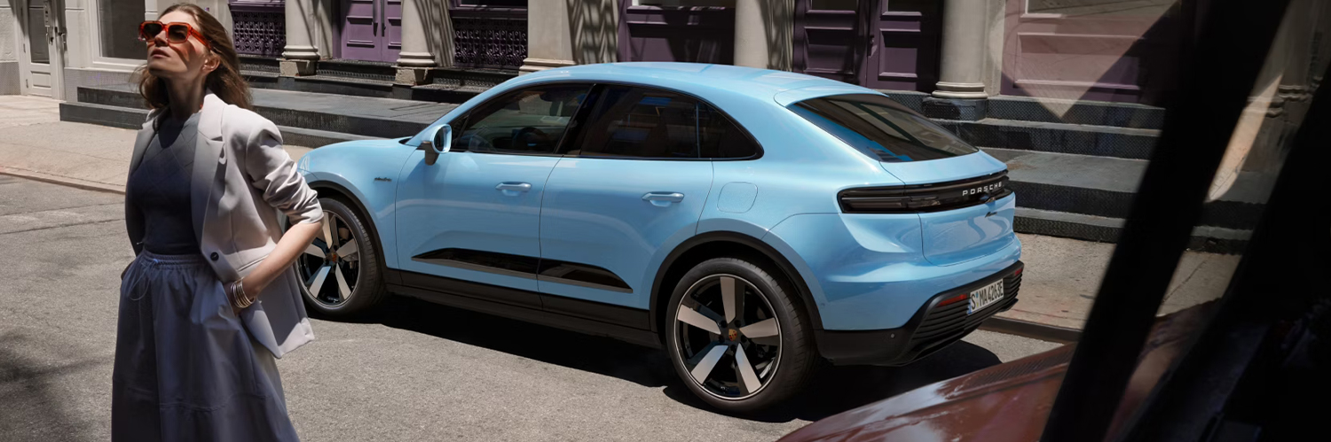 2025 Blue Porsche Macan parked outside with a stylish woman standing in front