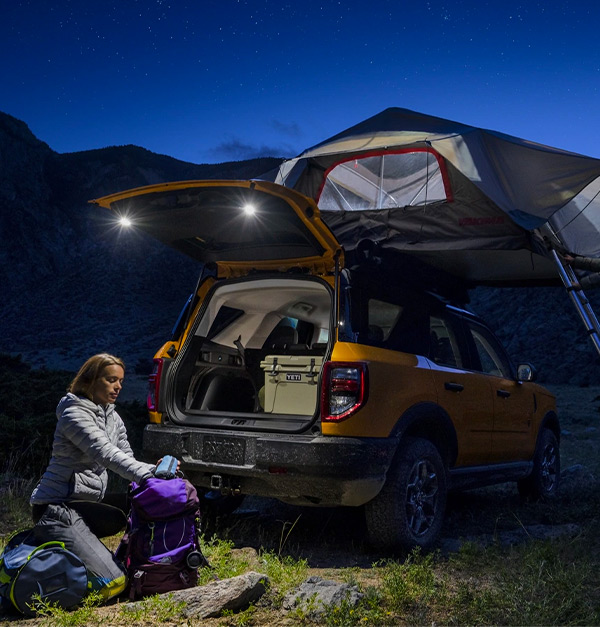 A woman using the 2021 Ford Bronco Sport rear flood lights to unpack in the middle of the night