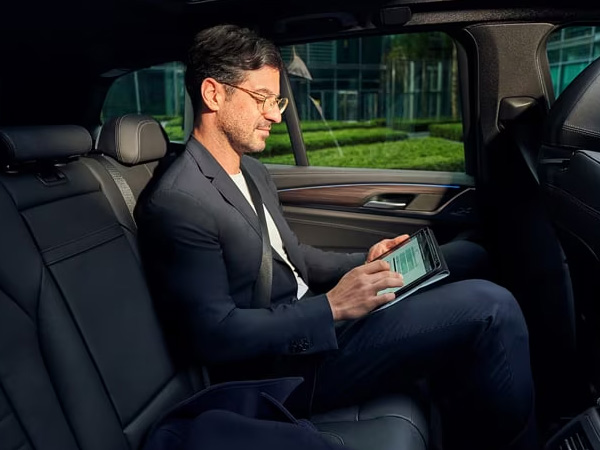 A man uses a tablet from the backseat of a BMW