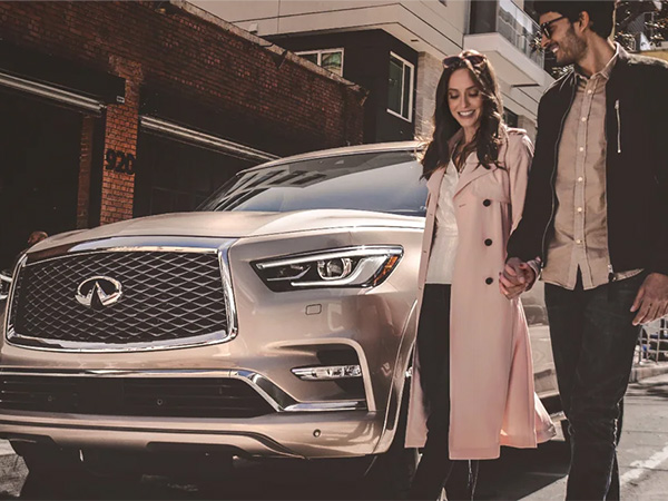 Two people holding hands walking beside an INFINITI