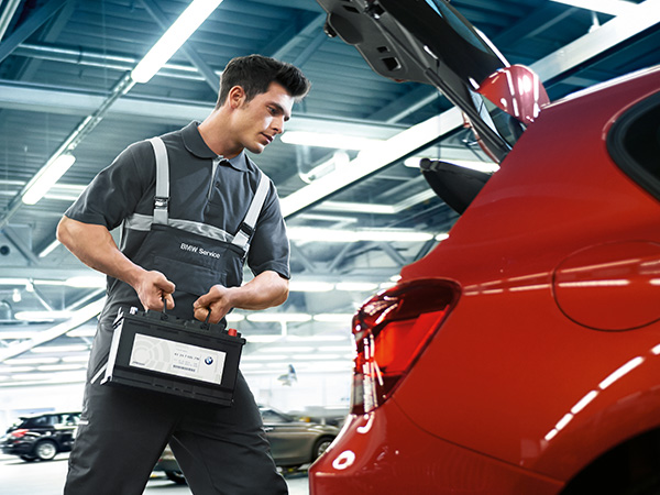 BMW service tech putting a battery in the trunk of a vehicle