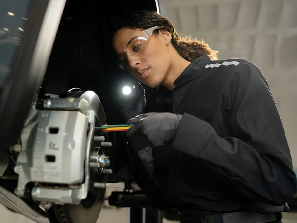 INFINITI service tech inspecting a vehicle's brakes with a light