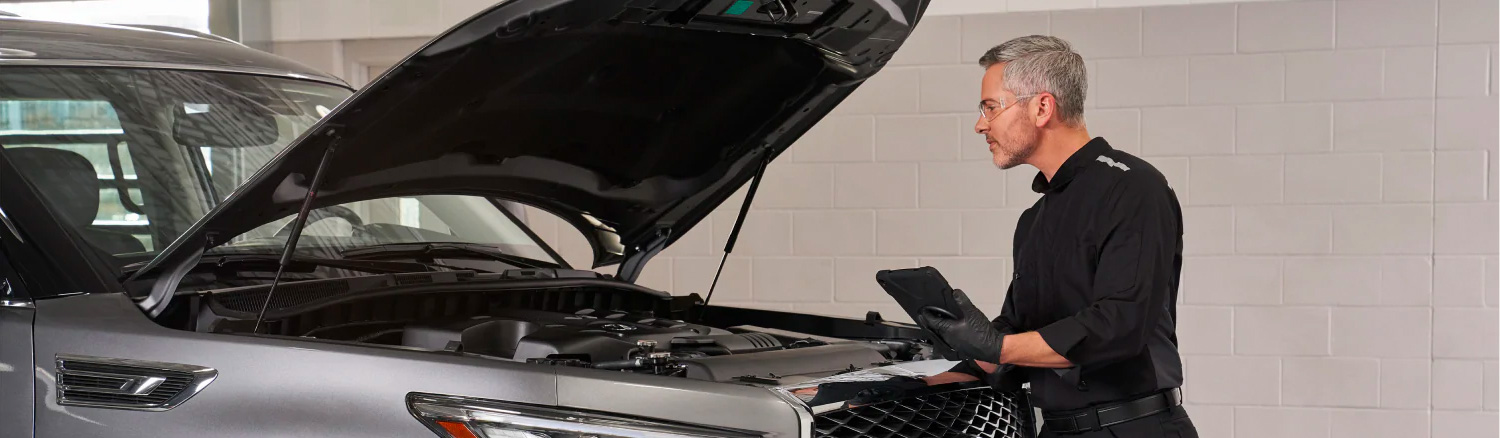 INFINITI service tech inspecting under the hood of a vehicle