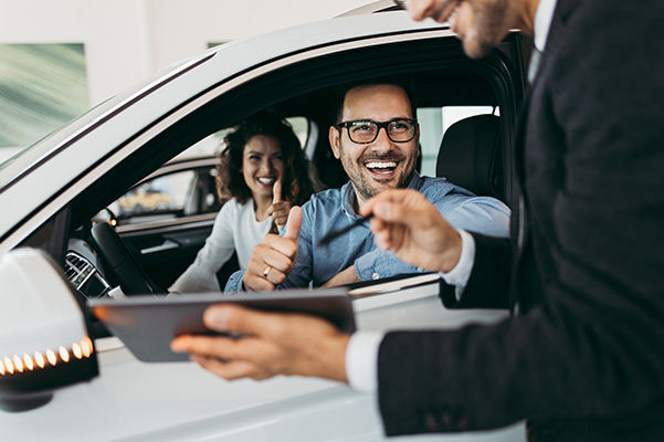 Happy couple in a car with salesman showing tablet