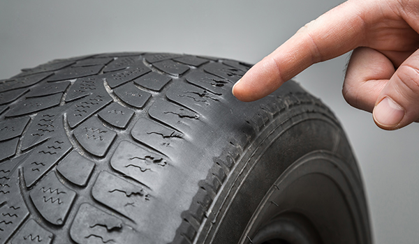 Man's hand finger pointing to the old, damaged and worn black tire tread. Change time. Tire tread problems and solutions concept.