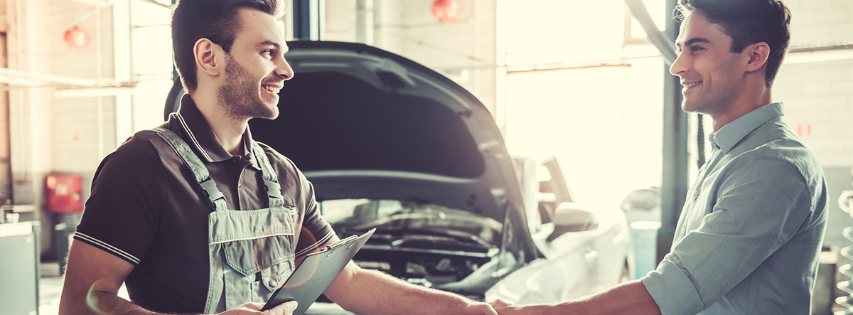 auto technician shaking hands with customer with a vehicle in the background with the hood open