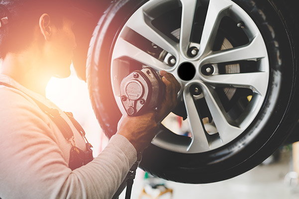 auto technician tightening wheel bolt using power drill