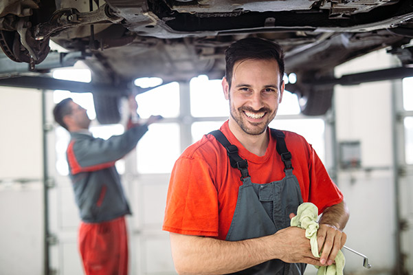 auto technician smiling with red t-shirt inspecting vehicle undercarriage