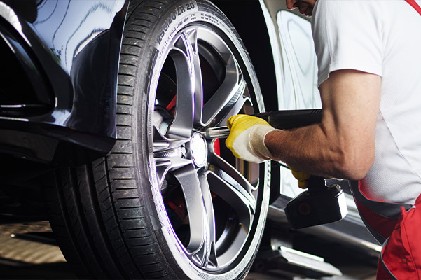 auto technician tightening wheel bolt using power drill