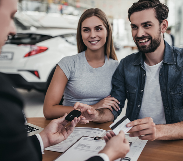 Happy couple filling out their car paperwork with an employee